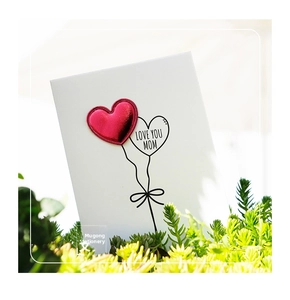 Detail of 3D red leather heart card with Love You Mom text placed in green plants