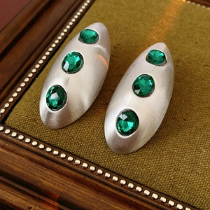 Close-up of matte silver oval earrings inlaid with three green oval gemstones