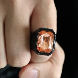 Detailed close-up of a black stainless steel ring featuring a vibrant orange square gemstone