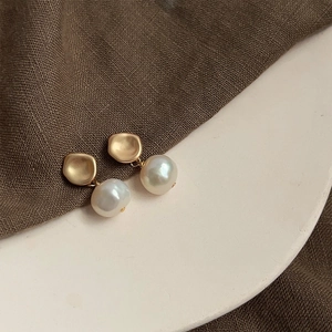 Detail of baroque pearl drop earrings featuring matte gold geometric studs on linen texture