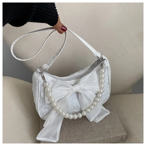 Close-up of white fashion handbag featuring a large ribbon bow and faux pearl handle strap