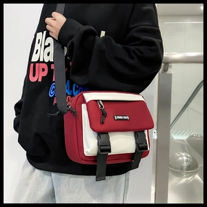 Street style shot of a red and white messenger bag with adjustable black strap and buckle