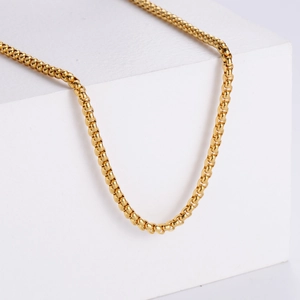 Polished 18K gold-plated square box chain necklace draped over a white stone block