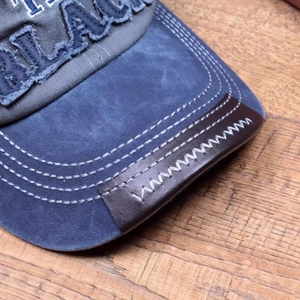 Close-up of dual-row stitching on vintage washed canvas cap with leather brim detail
