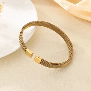 Dettaglio del bracciale rigido dorato con trama a rete e finitura minimalista moderna