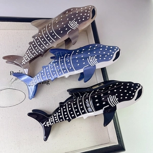 Three whale shark claw clips in blue, grey, and black on a white display cushion