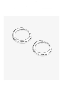 Macro shot of minimalist silver huggie hoop earrings featuring a polished metallic finish