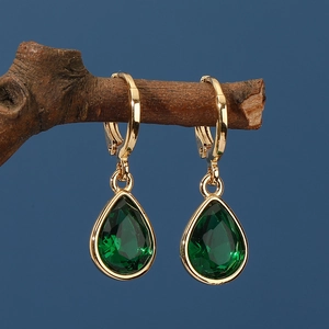 Elegant gold waterdrop earrings featuring deep green pear-cut stones on rustic wood branch