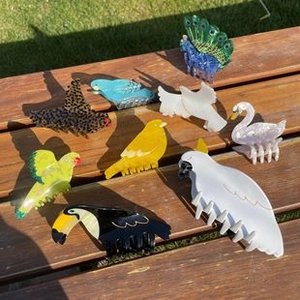 Detailaufnahme bunter Haarklammern aus Acetat in Vogelform auf einer Holzbank