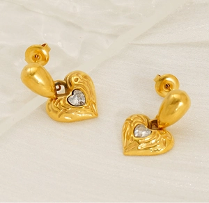 Detail of gold-plated heart earrings with radiant texture and centered clear rhinestone