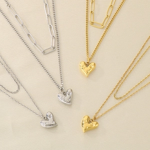 Détail de colliers superposés en or et argent avec des pendentifs en cœur texturés