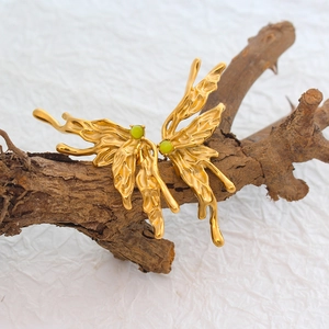 Artistic gold butterfly earrings with green stones on a dark wood display