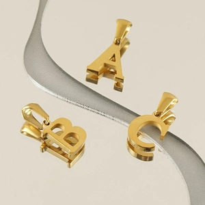 Close-up of golden A, B, C letter pendants with polished finish on a mirrored surface