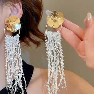 Detail showing elegant gold flower stud earrings with long white beaded crystal tassels
