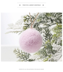 Detailed view of a pink wool felt Christmas ball ornament hanging on a snowy pine branch