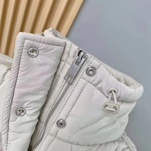 Close-up of beige quilted vest featuring metal zipper, silver buttons and adjustable drawstring