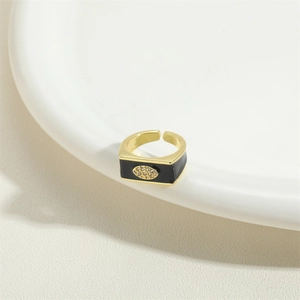 Close-up of golden rectangular ring with black enamel and sparkling evil eye design