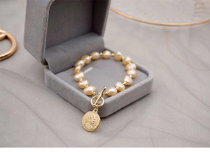 Detailed macro view of baroque pearl bracelet with gold coin pendant in a velvet box
