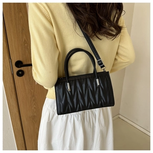 Detail of black pleated crossbody bag with wave quilting and silver hardware shown on model