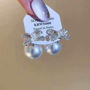 Macro shot of silver bow earrings with sparkling rhinestones and white pearls on card