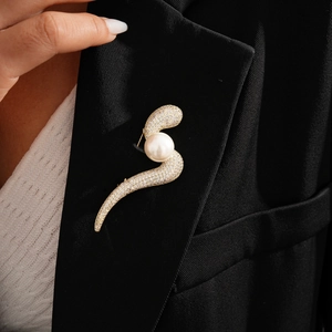 Detail of a 14k gold plated S-shaped brooch with cubic zirconia and pearl on a black suit