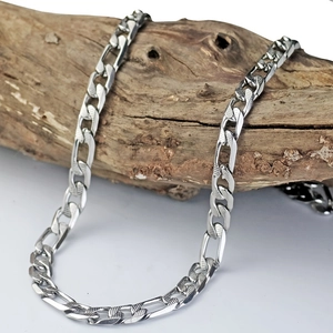Polished silver Figaro link chain necklace displayed on a textured natural wooden branch