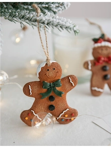 Close-up of resin gingerbread man ornament with green bow on snow-covered pine branch