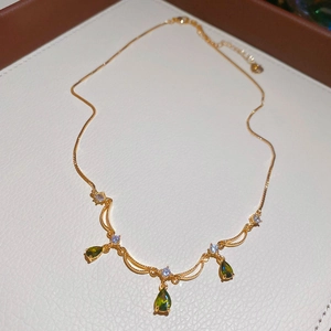 Dettaglio collana dorata con tre pietre a goccia verdi e piccoli zirconi trasparenti