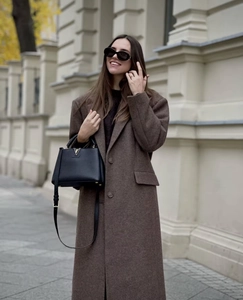 Chic long brown wool coat for women styled with black leather bag in urban city setting
