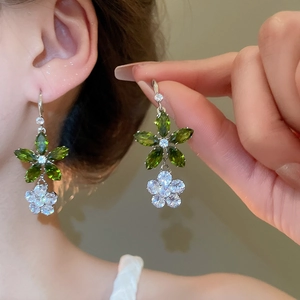 Détail de boucles d'oreilles fleur argentée avec cristaux de zircon vert et blanc