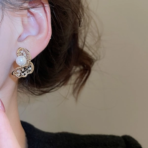 Detail of golden hollow butterfly earring with pearl and zircon worn on ear