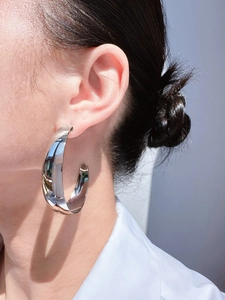 Detailed close-up showing the mirror-polished finish of the large silver C-shaped hoop earrings
