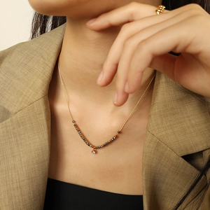 Elegant gold necklace with black faceted beads and zircon pendant worn on a brown blazer