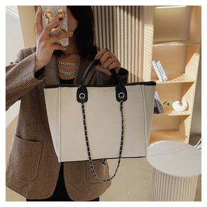 Detail of canvas tote bag featuring black leather handles and metal chain shoulder strap