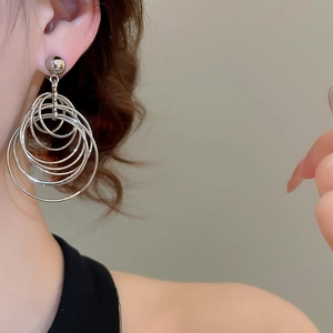 Detail view of silver multi-layer metal hoop earrings worn by a model in soft light