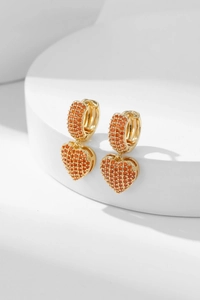 Detailed view of heart-shaped earrings with micro-pave orange zircon on a white stand