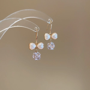 Close-up of zircon bow pearl earrings with gold hooks and sparkling crystal pendants