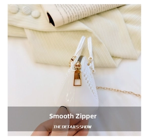 Detail shot of golden metal zipper and metallic chain strap on white mini pearl handbag