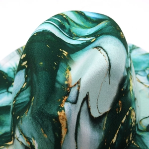Macro view of dark green marble pattern fedora hat with elegant gold leaf accents