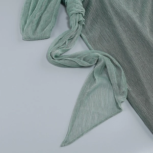 Gros plan sur un tissu plissé vert clair aux reflets métalliques et nœud élégant