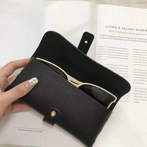 Detail of a minimalist black leather sunglasses pouch with a gold snap button closure