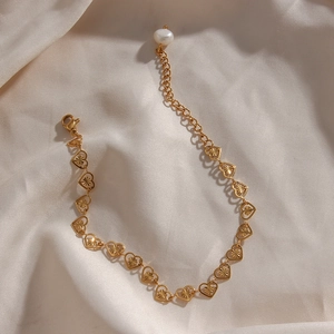 Detailed view of a gold heart chain bracelet with a white pearl charm on silk fabric
