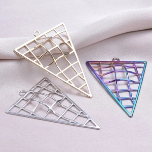 Macro shot of triangle metal charms in gold, silver, and rainbow on soft pink fabric