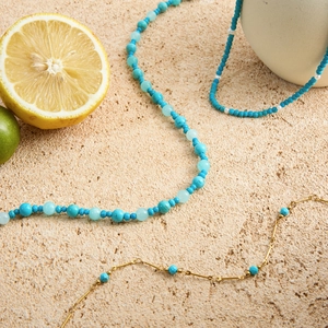 Close-up of 18K gold stainless steel chain layered with turquoise beaded necklaces