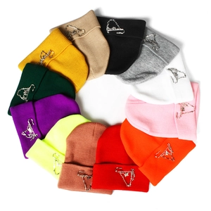 Various colored knit beanies with metal chains and pins arranged in a circle
