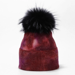 Detail of multi-color tie-dye knit beanie with large black fluffy faux fur pompom