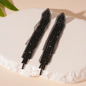 Detailed view of black rhinestone tassel earrings displayed on a white textured stone base