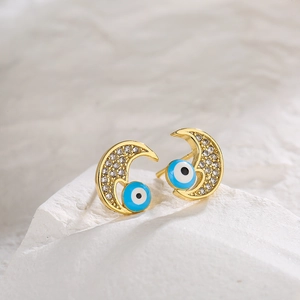 Gold-plated moon earrings with zircon and blue evil eye charms on a stone surface