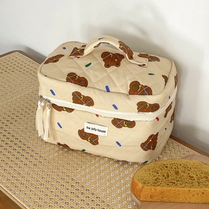 Detailed close-up of a beige quilted bear makeup bag with zipper and handle on a rattan bench