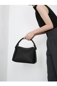 Close-up of black lychee grain leather handbag with top handle held by a model